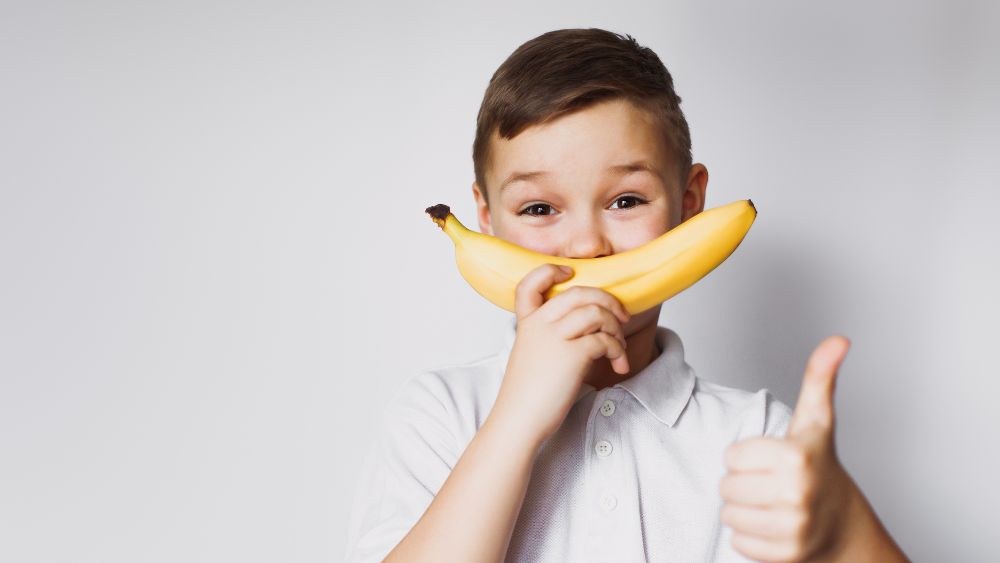 Child holding a banana and giving thumbs up.